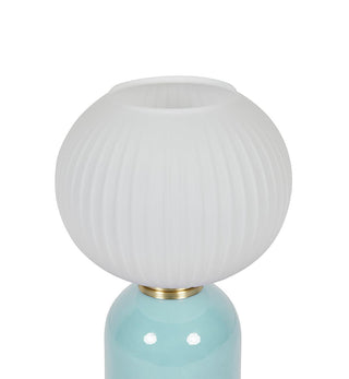 A close-up of a table lamp featuring a ribbed, frosted white glass globe shade and a glossy light blue ceramic base with a brass neck ring, set against a plain white background.